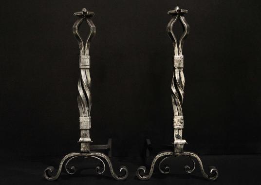 A large pair of polished wrought iron firedogs