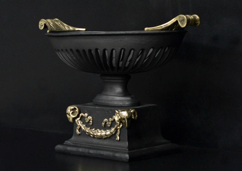 A cast iron bowl grate with brass rams heads