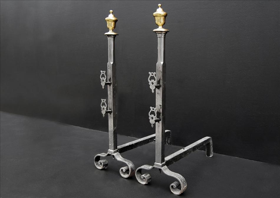 A pair of polished steel firedogs with brass urn finials