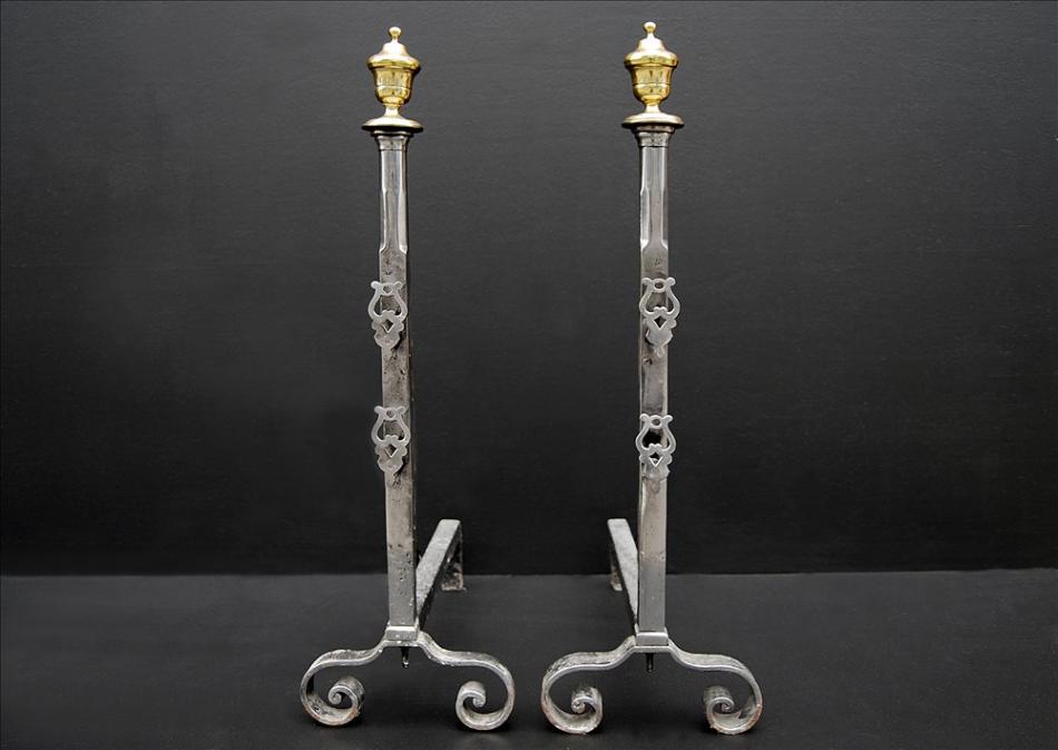 A pair of polished steel firedogs with brass urn finials